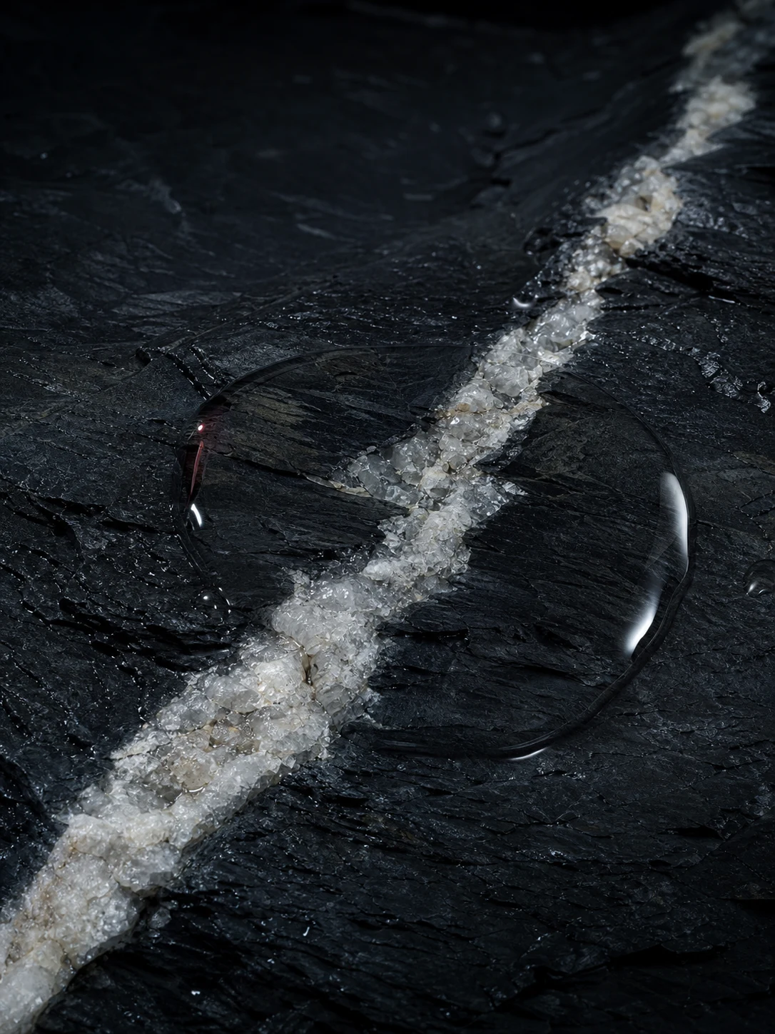 Art-directed study of clear water pooled over a quartz seam in dark mineral rock